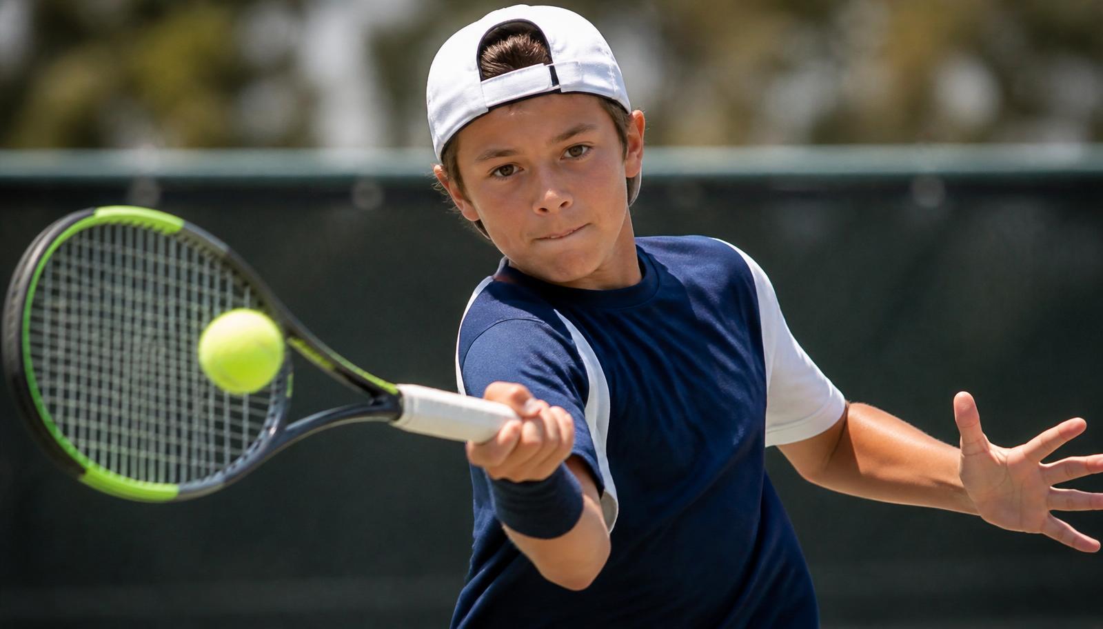 Junior player mid-forehand at the moment of contact, ball visible